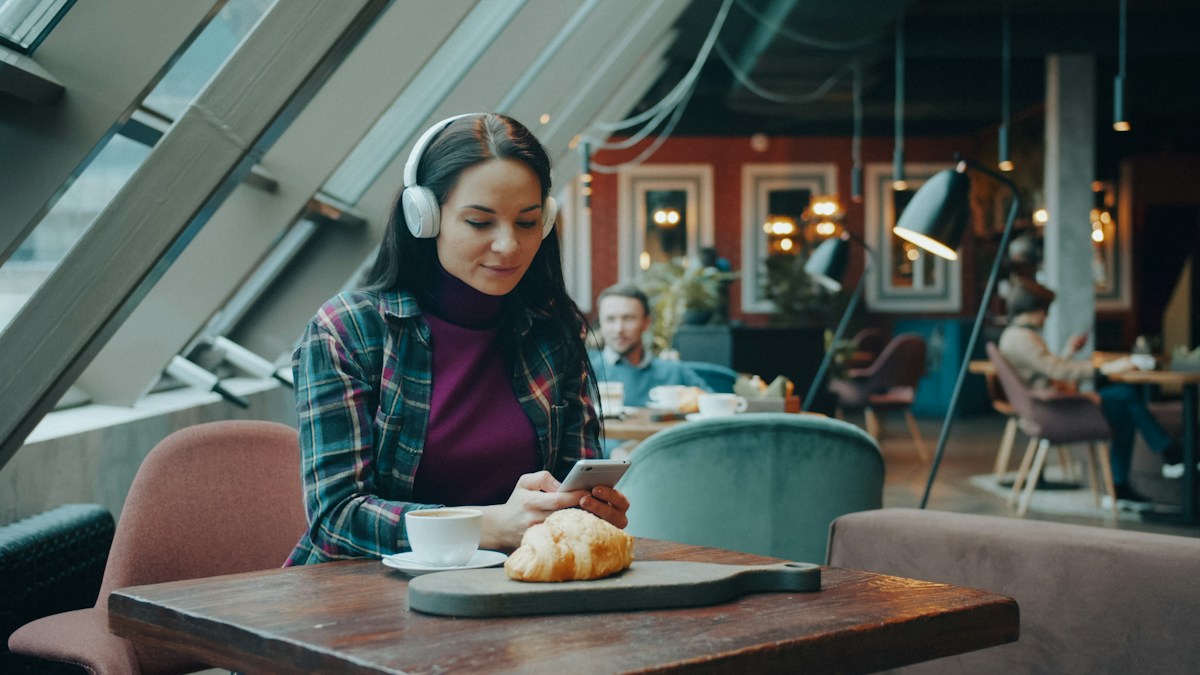 A woman wearing headphones and practising on her phone in a café